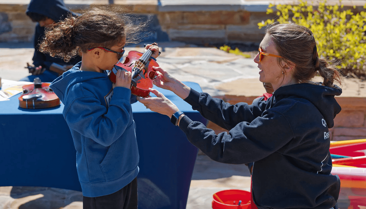 A child trying a violin with an adult at an instrument petting zoo